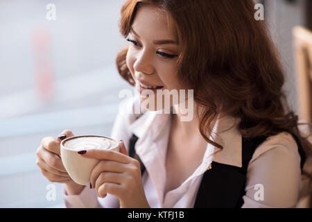 Young smiling redhead woman drinking cappuccino au café. Banque D'Images