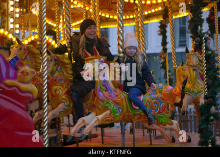 Pluie et vent saluer la dernière minute la veille de Noël Noël les visiteurs de la ville dans le fayre George Square. Mère et fille ride le carrousel merry go round Banque D'Images