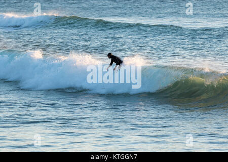 Surfer sur la plage de Fistral, Newquay, Cornwall, UK dans une mer froide au coucher du soleil