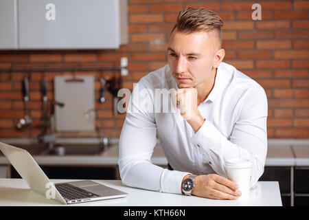 L'homme travaillant à domicile sur certains projet, assis à table blanche looking at laptop
