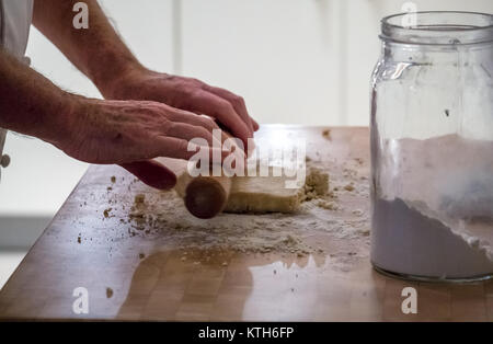 Close up de plus dans les blancs chef pâte de roulement avec un rouleau à pâtisserie faire sur un bloc de bois avec un pot de farine dans une cuisine Banque D'Images