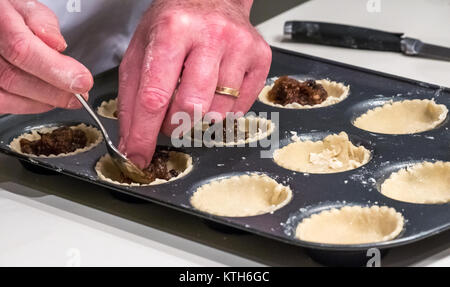 Close up of man's hands avec anneau de mariage dragées mince pie cas prêt à cuire avec la viande hachée sur un comptoir de cuisine pour Noël blanc Banque D'Images