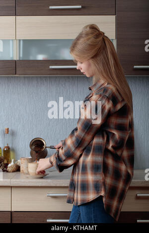 Belle jeune femme dans une chemise à carreaux marron, se verse dans la tasse de café . Cuivre ancienne cafetière et tasse en céramique. Banque D'Images