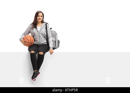 Teenage girl with a basket-ball et un sac à dos assis sur un panneau isolé sur fond blanc Banque D'Images