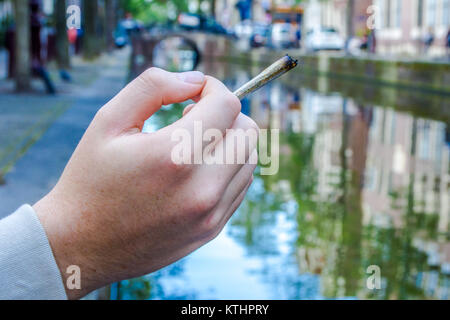 Main tenant un joint de cannabis sur un canal à Amsterdam Banque D'Images