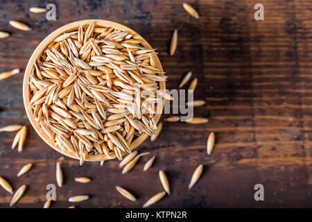 Close up image d'un bol en bois plein de grains d'avoine sur table en bois foncé Banque D'Images