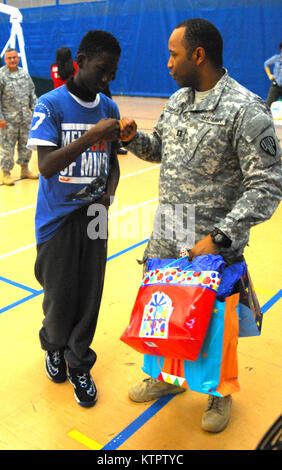 Le capitaine Oyeyemi Daramola, 369e brigade de maintien en puissance, remet un cadeau à un enfant de l'Harlem Children's Zone durant un jouet et enduire à l'événement d'entraînement Harlem Armory, le 5 décembre 2015. L'événement était organisé comme un moyen pour le 369e brigade de maintien en puissance de donner en retour à la communauté dans laquelle l'unité a ses racines. (US Army National Guard photo par le Sgt. Jeremy Bratt, 369e Brigade de soutien/libérés) Banque D'Images