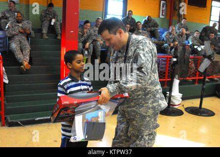 Capitaine John Mancini, 369e brigade de maintien en puissance, remet un cadeau à un enfant de l'Harlem Children's Zone durant un jouet et enduire à l'événement d'entraînement Harlem Armory, le 5 décembre 2015. L'événement était organisé comme un moyen pour le 369e brigade de maintien en puissance de donner en retour à la communauté dans laquelle l'unité a ses racines. (US Army National Guard photo par le Sgt. Jeremy Bratt, 369e Brigade de soutien/libérés) Banque D'Images