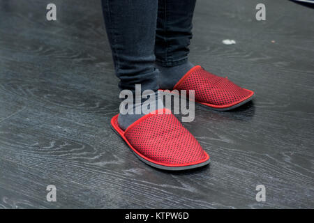 Close up parquet en bois sombre et pieds en rouge chaussons sentiment confortable Banque D'Images