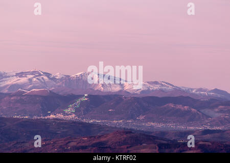 La vallée de l'Ombrie en hiver, avec une vue de la ville de Gubbio, avec de grands arbres de Noël éclairé sur le flanc de la montagne et Monte Cucco recouvert de neige Banque D'Images