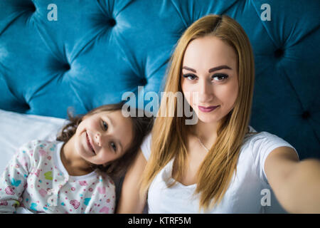 Mother and Daughter lying on bed and taking self portrait avec le smartphone. Femme tenant une petite fille avec des selfies dans la chambre. Banque D'Images