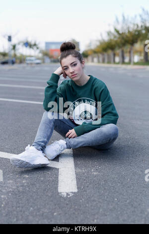 Teen girl assis sur le plancher d'un garage de stationnement. Tir vertical avec lumière naturelle. Banque D'Images