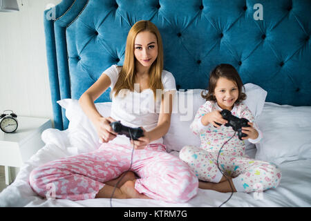 Mère et fille joue à des jeux vidéo sur la console de jeux à la maison de lit Banque D'Images