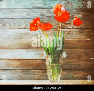 Bouquet de fleurs tulipes rouges dans un vase en verre sur un fond de bois conseils grange. Gros plan retro photo teinté Banque D'Images