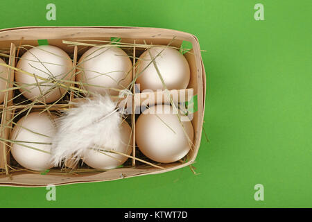 Six oeufs de poule ferme blanc frais dans le récipient en bois fort avec hay et plumes sur fond vert, augmentation de la vue supérieure, juste au-dessus Banque D'Images