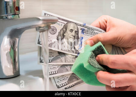 Un homme se frotte une éponge hundred dollar bill. Le blanchiment, Concept. lavage de l'argent sur le marché noir. Billets de 100 dollars dans les mains de Banque D'Images