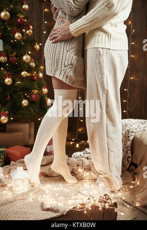 Les jambes de jeune couple dans un intérieur en bois sombre avec des lumières, lanterne à bougie. Man and Woman hugging. Maison de vacances de nouvel an. Les lumières de Noël et de décoration. Dr Banque D'Images