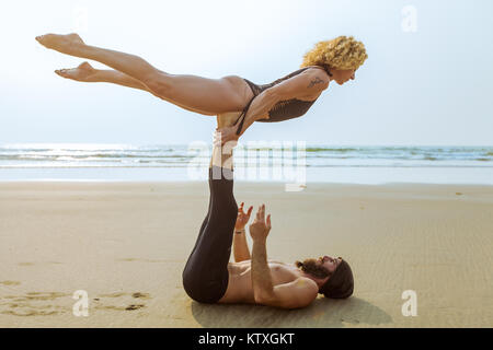 Deux belles personnes pratiquant le yoga acro sur la plage au coucher du soleil à Goa, Inde Banque D'Images