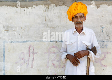 Vieil indien homme en blanc tenue le port du turban orange, debout devant un mur blanc dans un village près de Pushkar, Rajasthan, Inde. Banque D'Images