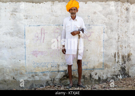 Vieil indien homme en blanc tenue le port du turban orange, debout devant un mur blanc dans un village près de Pushkar, Rajasthan, Inde. Banque D'Images