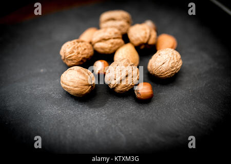 Fruits entiers mixtes dans leurs coquilles, y compris les noix, noisettes, amandes et noix de pécan tourné sur ardoise noire Banque D'Images