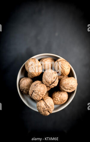 Un bol de noix dans leurs coquilles dans un bol tourné à partir de ci-dessus, sur un fond d'ardoise noire naturelle Banque D'Images