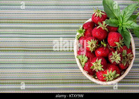 Les fraises sucrées mûrs dans panier en osier et de feuilles de menthe sur fond de bois Banque D'Images