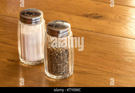 Close up de salière et poivrière en verre ou des pots de sel et de poivre sur une table en bois ,très commun coin condiments vu sur n'importe quelle table aux heures des repas Banque D'Images