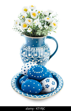 Plaque en céramique bleue avec des oeufs de Pâques peints et fleurs dans vase correspondant sur fond blanc Banque D'Images