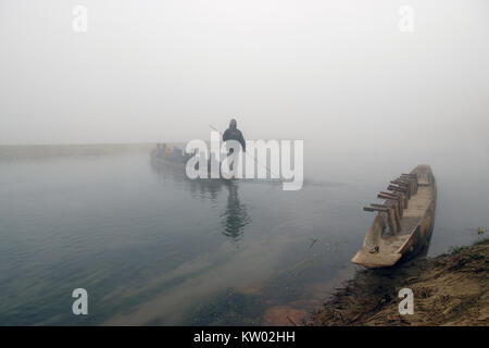 Plus tôt le matin sur la rivière : un canot en bois se trouve à la rive, avec des gens un autre canot flotte au loin dans le brouillard, un transporteur avec une rame. Banque D'Images