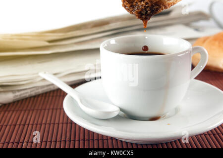 Un croissant trempé dans une tasse de café pendant un petit-déjeuner, un journal sur l'arrière-plan. Banque D'Images