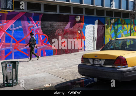 Une fille passe devant un mur avec l'art de rue dans East Harlem sur un après-midi ensoleillé. Banque D'Images