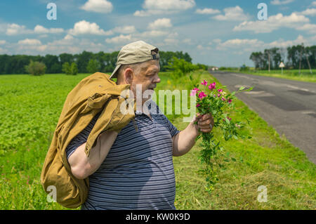 Man avec sack et bouquet de fleurs sauvages debout sur une route au centre de l'Ukraine Banque D'Images
