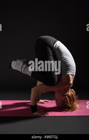 Young woman practicing yoga, Sirsasana / Charge Wavecrest poser Banque D'Images