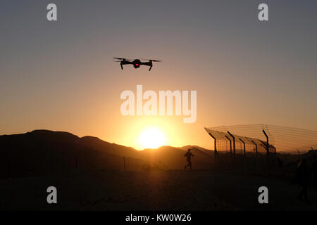 Un appareil radio controlled quadcopter drone survolant la silhouette d'un homme qui court à une position de défense de l'armée israélienne sur une colline stratégique dans l'ouest de la vallée de la plaine connue en hébreu comme Arava ou Aravah qui fait partie de la frontière entre Israël et la Jordanie. Banque D'Images