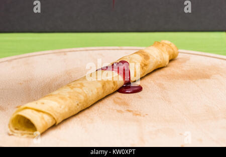 Crêpe roulé, Fédération de blinis avec confiture renversé sur une planche à découper en bois Banque D'Images