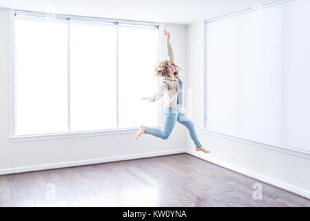 Une jeune femme heureuse de sauter jusqu'à moderne vide nouvelle chambre avec du parquet et de grandes fenêtres ensoleillées dans l'appartement Banque D'Images