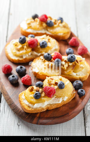 Crostini avec ricotta, Poires poêlées, noix et miel, décoré avec des framboises et bleuets Banque D'Images