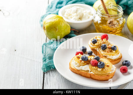 Crostini avec ricotta, Poires poêlées, noix et miel, décoré avec des framboises et bleuets Banque D'Images