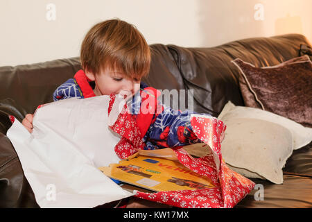 Tout-petit s'assit sur un canapé dans sa robe de l'ouverture d'un présent le matin de Noël Banque D'Images