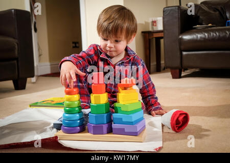 Tout-petit s'assit sur le plancher dans son pyjama jouant avec des jouets le matin de Noël Banque D'Images