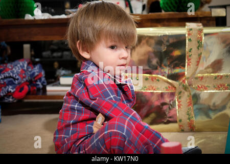 Tout-petit s'assit sur le plancher dans son pyjama jouant avec des jouets le matin de Noël Banque D'Images