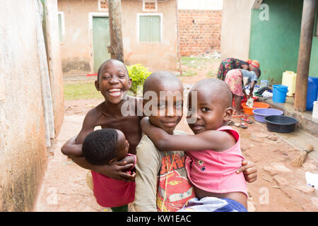 Lugazi, en Ouganda. 09 juin 2017. Les jeunes garçons africains tenant leurs frères et sœurs dans leurs bras. Les filles dans l'arrière-plan sont lave-linge dans des bassins. Banque D'Images