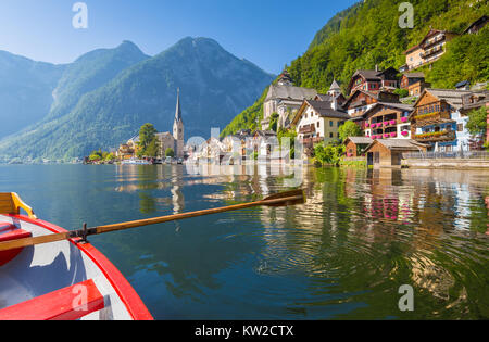 Carte postale panoramique vue du célèbre village au bord du lac de Hallstatt dans les Alpes autrichiennes avec barque traditionnelle en bois dans la belle lumière du matin sur une Sun Banque D'Images