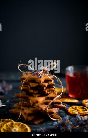 En forme d'étoile de pile liée gingerbread cookies et un verre tasse de thé rouge. Décorées avec des fleurs séchées, et les tranches d'orange. Banque D'Images