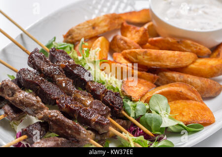 Les brochettes d'agneau sur salade avec des quartiers de pommes de terre et crème fraîche Banque D'Images