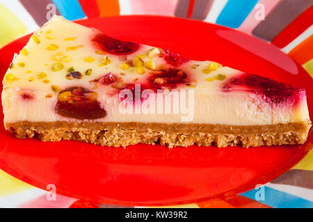 Tesco finest & Framboise cheesecake Pistache tranche sur la plaque de couleur rouge Banque D'Images