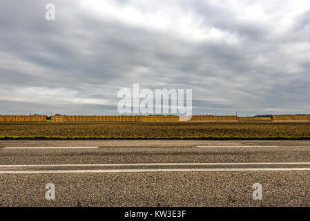 Route asphaltée en face d'un champ avec un long mur de tas de foin Banque D'Images