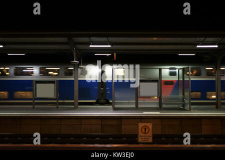La plate-forme de la gare de Weinheim en soirée avec des sièges sur une cloison de verre mur et un train qui passe. Banque D'Images