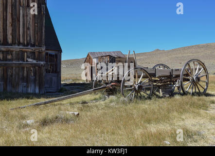 Une ancienne grange, outhouse, de wagons et de hautes herbes, avec une colline, la prairie ouverte, et ciel bleu profond dans l'arrière-plan, dans l'historique ville fantôme, Bodie Banque D'Images